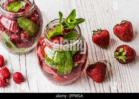 Detox Wasser mit Beeren auf weißem Hintergrund aus Holz. Gesunde Getränke Stockfoto