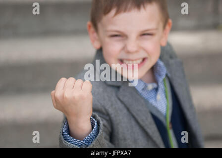 Kleiner Junge Jacke und Pullover mit Grimasse auf seinem Gesicht tragen droht mit der Faust Stockfoto