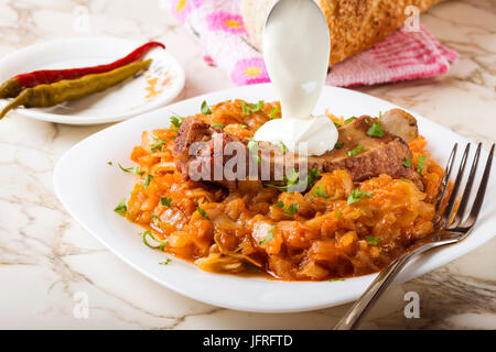 Kohl-Eintopf mit geräuchertem Schweinefleisch Rippen, Creme und grün Petersilie serviert in weißen Teller mit eingelegtem Chili Paprika und Brot Stockfoto