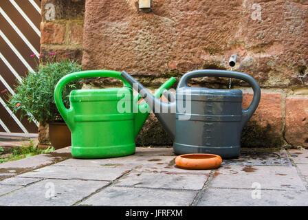 Zwei Kunststoff-Gießkannen, grün und grau, bereit für gießen den Garten stehen auf dem Stein Pflaster in der Nähe der Wand, Heidelberg, Deutschland. Stockfoto