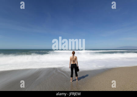 Junge Frau auf einem Sandstrand stehen und warten auf den Wellen, Almadraba de Monteleva, Almeria, Andalusien, Spanien. Stockfoto