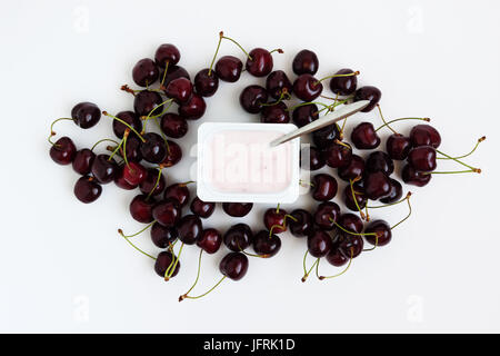 Container mit Joghurt und ein paar frische Kirsche Beeren auf weißem Hintergrund, isoliert, Ansicht von oben. Stockfoto