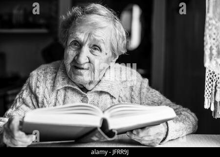 Ältere Dame, ein Buch lesen, sitzt am Tisch. Schwarz-weiß-Foto. Stockfoto