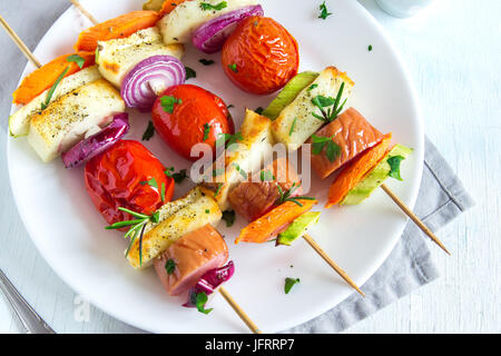 Gegrillte Wurst und Gemüse-Spieße mit frischen Kräutern auf weißen Teller Stockfoto