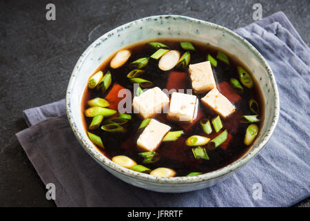 Japanische Miso-Suppe in Keramikschale auf schwarzen Steintisch, Textfreiraum. Asiatische Miso-Suppe mit Tofu. Stockfoto