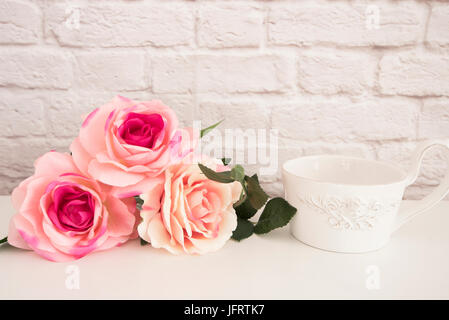 Strauß Rosen auf einem weißen Tisch, eine große Tasse Kaffee im vorderen Engel, romantischen floral frame Hintergrund, floralen Stil Wall Mock Up, Rose Blume Mock Stockfoto