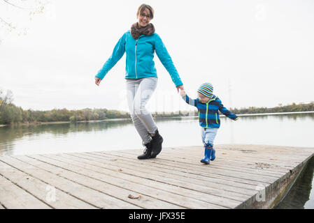 Lächelnde Mutter und Sohn gehen auf Holzsteg über See Stockfoto