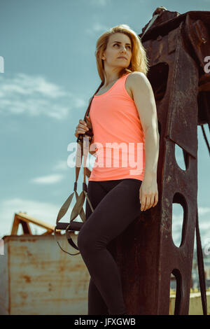 Schöne junge Frau in einem Orangen T-shirt mit Trx-Fitness-Riemen Stockfoto