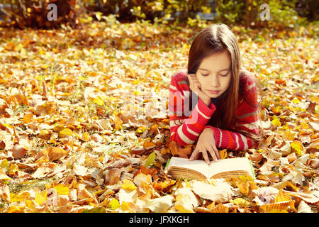 Teenager-Mädchen auf Laub im Park liegen und ein Buch zu lesen. lernen und Bildung im Herbst Stockfoto