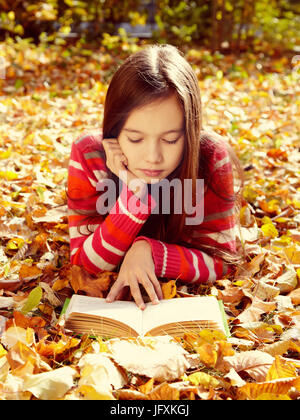 Teenager-Mädchen auf Laub im Park liegen und ein Buch zu lesen. lernen und Bildung im Herbst Stockfoto