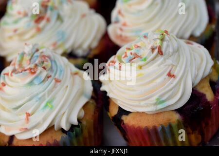 Der Blick auf die Platte des Weiß Creme Muffins mit bunten Bonbons auf der Oberseite Stockfoto