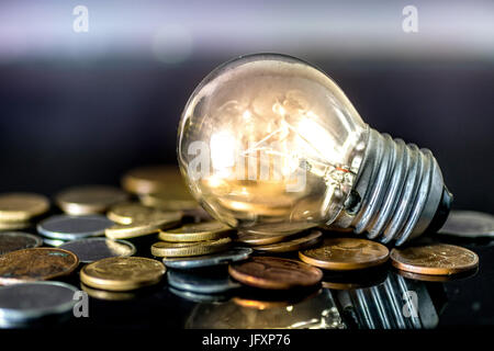 Gelbe Glühbirne auf Haufen von Münzen - Geld, Finanzen, Ersparnisse Konzept und Idee Stockfoto