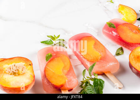 Sommer Desserts. Frozen Drinks serviert. Süße Frucht Eis am Stiel aus gefrorenen Pfirsich Tee mit Minze. Auf einem weißen Marmortisch mit Zutaten - Pfirsich, Minze, Eis. Stockfoto