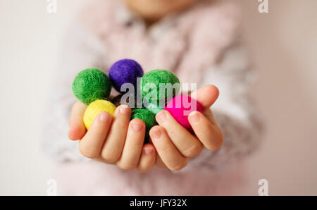 Nahaufnahme von Kindern Händen mit bunten Filzkugeln. Kind, Kind-Palmen. Ein kleines Mädchen denken Sie Handvoll farbiger Wolle Kugeln. Lifestyle-Konzept. Sel Stockfoto