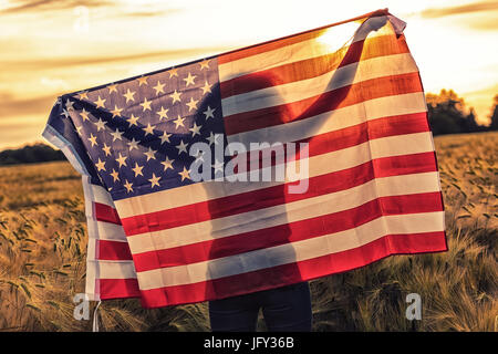 Silhoette des African American Mädchen Teenager weibliche junge Frau im Bereich der Weizen oder Gerste Getreide hält USA Sternenbanner Fahne im goldenen Sonnenuntergang e Stockfoto