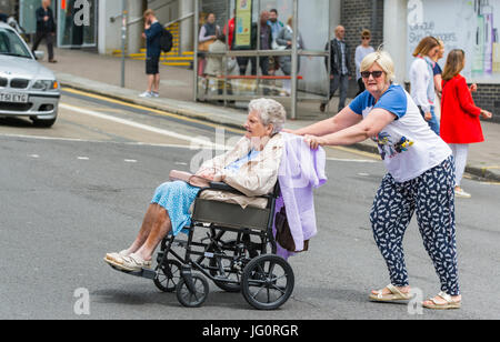 Frau drücken eine ältere Frau in einem Rollstuhl über eine Straße. Stockfoto