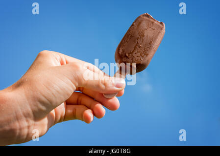 Hand hält eine Eis Creme Schokolade Eis am Stiel auf blauen Himmelshintergrund Stockfoto