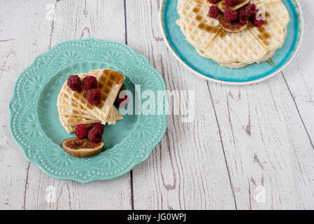 Hausgemachte weichen belgischen herzförmige Waffeln mit Himbeeren und Feigen, mit Honig auf türkis blaue Platte bedeckt. Rustikale Holz Hintergrund, Ansicht von oben. Stockfoto