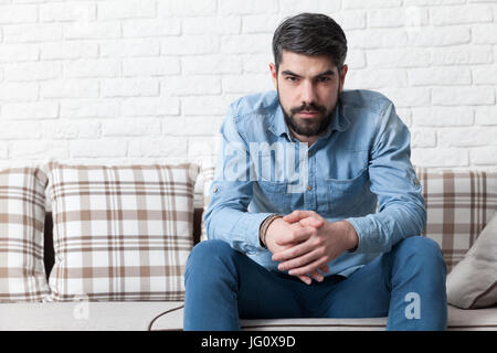 Kamera schaut zuversichtlicher junger Mann sitzt auf einem Sofa, während. Stockfoto