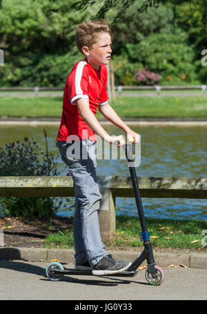 Junge auf einem Roller durch einen Park fahren. Stockfoto