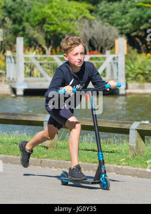 Junge auf einem Roller durch einen Park fahren. Stockfoto