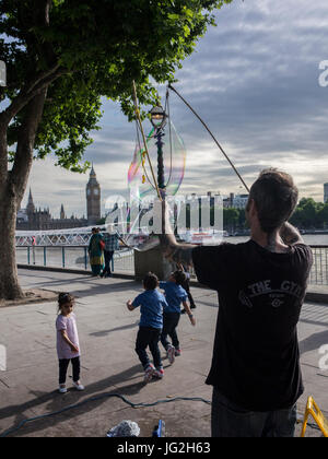 Eine Straße Straßenmusiker bläst Luftblasen am Südufer der Themse in London mit der Houses of Parliament und Big Ben im Hintergrund Stockfoto