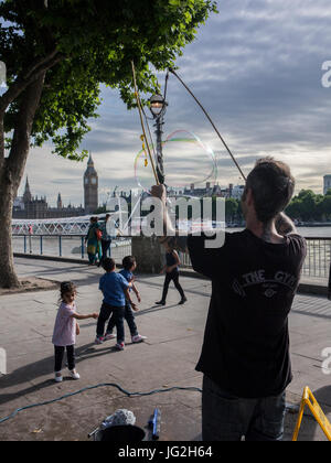 Eine Straße Straßenmusiker bläst Luftblasen am Südufer der Themse in London mit der Houses of Parliament und Big Ben im Hintergrund Stockfoto