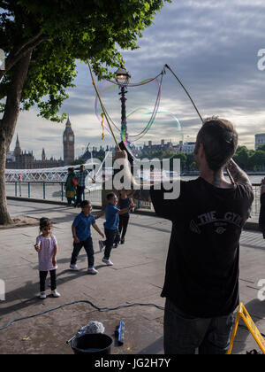 Eine Straße Straßenmusiker bläst Luftblasen am Südufer der Themse in London mit der Houses of Parliament und Big Ben im Hintergrund Stockfoto