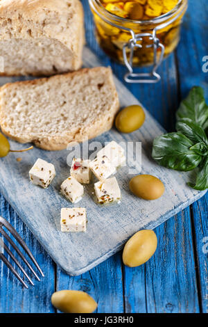 Käsewürfel, gewürzt mit Kräutern auf blauem Hintergrund aus Holz Stockfoto