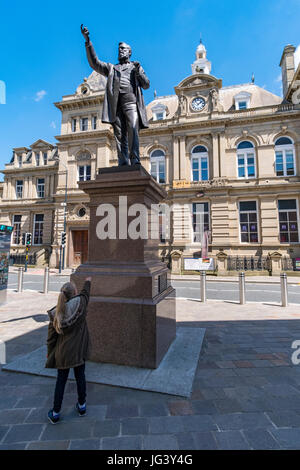 Ein kleines Mädchen imitiert die Pose einer Statue des W. E. Forster, die vor einem Eingang zu der Broadway Shopping Centre in Bradford gelegt wird. Stockfoto