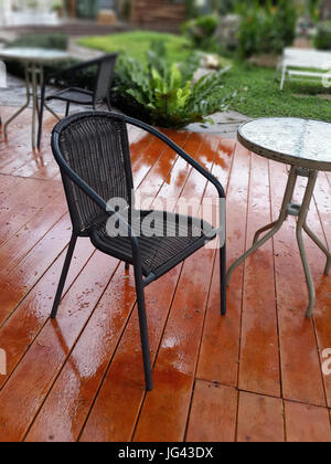 Schwarzer Stuhl und Teetisch auf Holzterrasse im Garten in der Regenzeit. Stockfoto