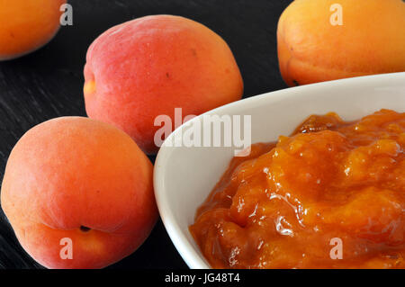 Marillenmarmelade und Aprikosen auf schwarzem Hintergrund aus Holz Stockfoto