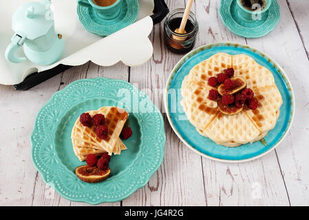 Weiche belgische Waffeln mit Himbeeren und Feigen, in Herzform mit Honig auf türkis blaue Platte bedeckt. Ein Tablett mit Kaffee und Kaffeemaschine ausgestattet. Leichten Rost Stockfoto