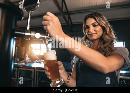 Junge Frau, die Abgabe von Bier in einer Bar aus Metall Zapfen. Schöne weibliche Barkeeper Antippen Bier in der Bar. Stockfoto