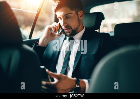 Junger Geschäftsmann telefonieren mit Handy und TabletPC verwenden, beim Sitzen auf dem Rücksitz eines Autos. Kaukasische männliche Führungskraft Reisen durch ein t Stockfoto