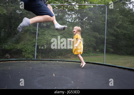 Kleine Mädchen in gelbem Kleid springen auf dem Trampolin Stockfoto