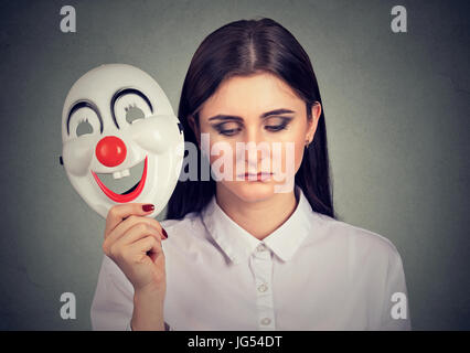 Porträt traurige Frau ausziehen Clownsmaske mit dem Ausdruck Glück auf graue Wand Hintergrund isoliert Stockfoto