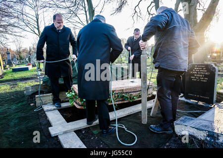 Eine Gruppe von Männern, die einen wicker Sarg mit Seilen, wie es in einem Grab gesenkt, auf einem Friedhof in England, Großbritannien. Stockfoto