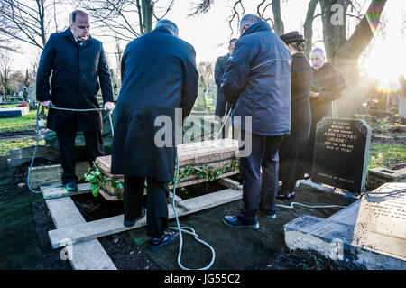 Eine Gruppe von Männern, die einen wicker Sarg mit Seilen, bereit, in ein Grab auf einem Friedhof in England, UK abgesenkt werden. Stockfoto