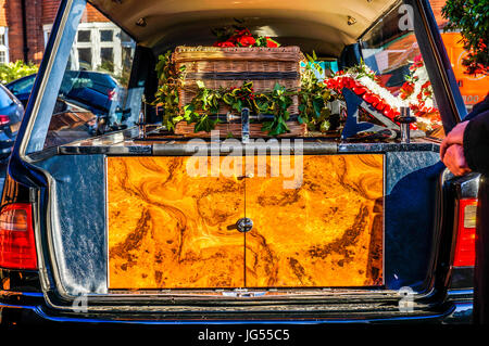 Eine enge Schuss von Wicker Sarg und floral Tribute auf dem Display in einem Leichenwagen, mit der Heckklappe öffnen. Stockfoto