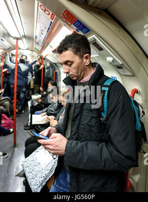 Weißer Mann in Freizeitkleidung mit einem Smartphone während der Verwendung der Londoner U-Bahn öffentliche u-Bahn Stockfoto