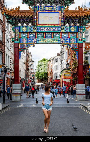 Ein junger japanischer Tourist posiert für ein Foto unter dem neuen Chinatown-Tor in der Wardour Street, Eingang zu Chinatown, London, UK Stockfoto