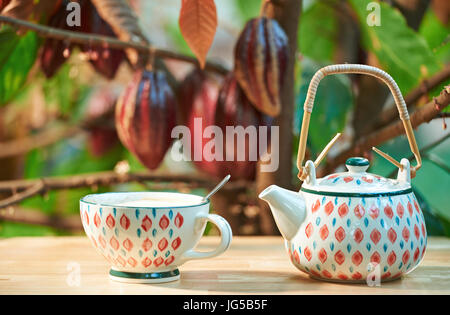 Heiße Schokolade im Cup auf Holztisch mit unscharfen Kakaobaum Zweig und Schoten Hintergrund Stockfoto