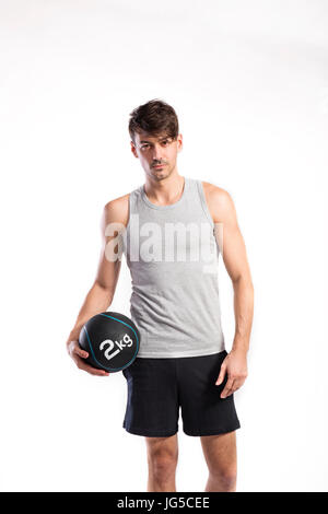 Hübsche Hipster Fitness Mann im grauen Tanktop-Shirt und schwarzen Hosen halten Medizinball. Studio auf weißem Hintergrund gedreht. Stockfoto