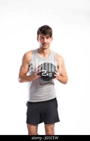 Hübsche Hipster Fitness Mann im grauen Tanktop-Shirt und schwarzen Hosen halten Medizinball. Studio auf weißem Hintergrund gedreht. Stockfoto