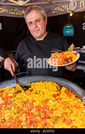 Ein spanischer Mann serviert frisch zubereitete Paella an einem Marktstand. Stockfoto