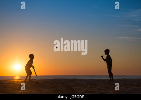 Zwei Jungen spielen Cricket am Strand, als die Sonne, Devon UK untergeht Stockfoto