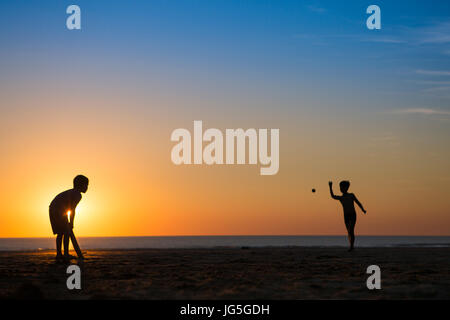 Zwei Jungen spielen Cricket am Strand, als die Sonne, Devon UK untergeht Stockfoto