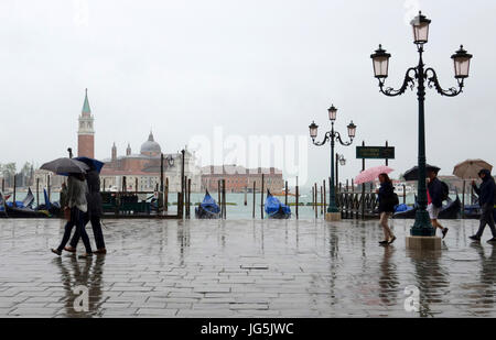 Menschen mit Regenjacken und Schirme an einem regnerischen Tag entlang der Riva Degli Schiavoni aus dem Palazzo Ducle, Venedig, Veneto, Italien Stockfoto