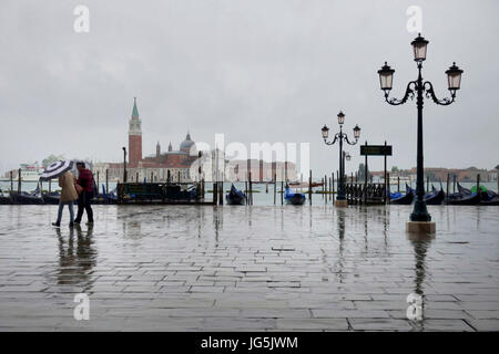 Menschen mit Regenjacken und Schirme an einem regnerischen Tag entlang der Riva Degli Schiavoni aus dem Palazzo Ducle, Venedig, Veneto, Italien Stockfoto